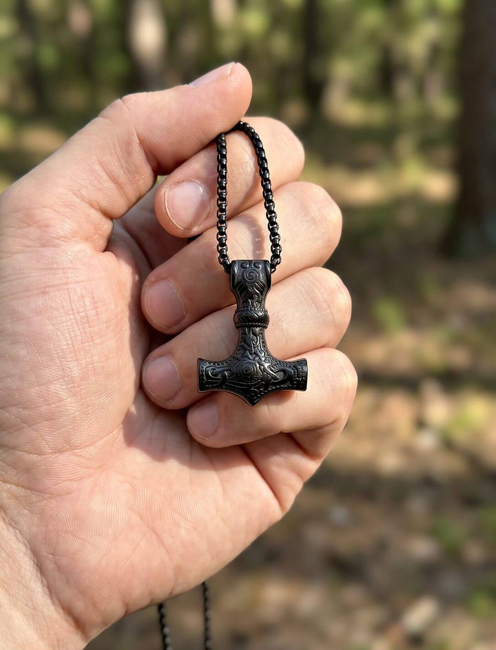 Hand hält den Wikinger-Anhänger an der Kette und zeigt seine Größe von etwa 3,5 cm vor unscharfem Wald