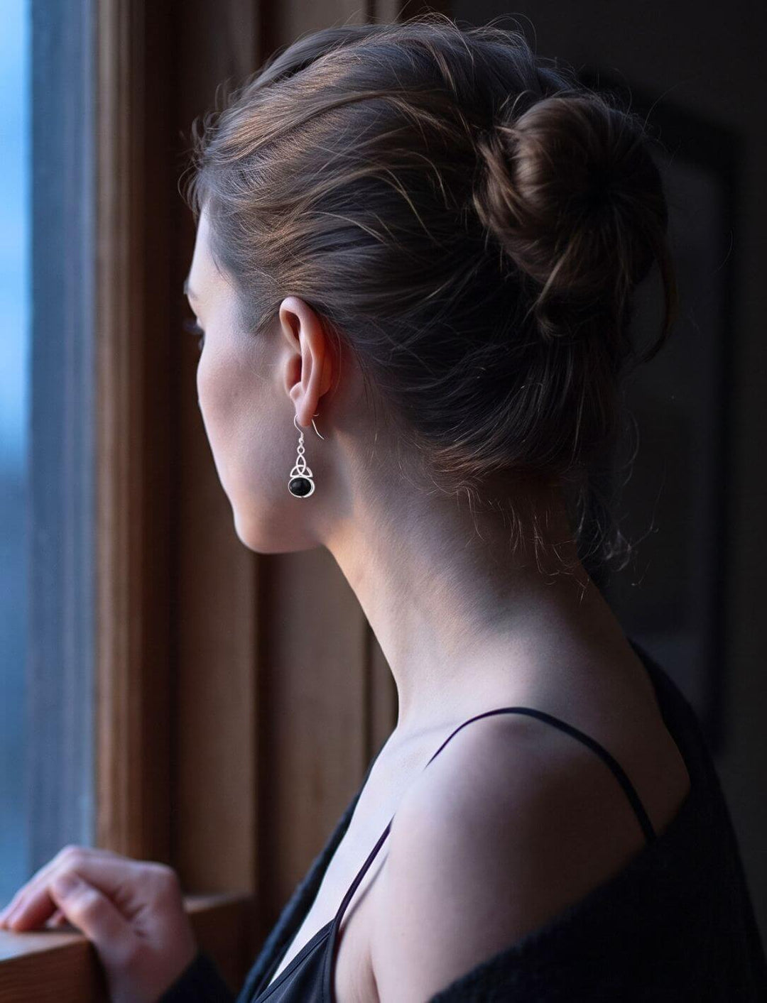 Frau mit Onyx Ohrhänger am Fenster in der blauen Dämmerung