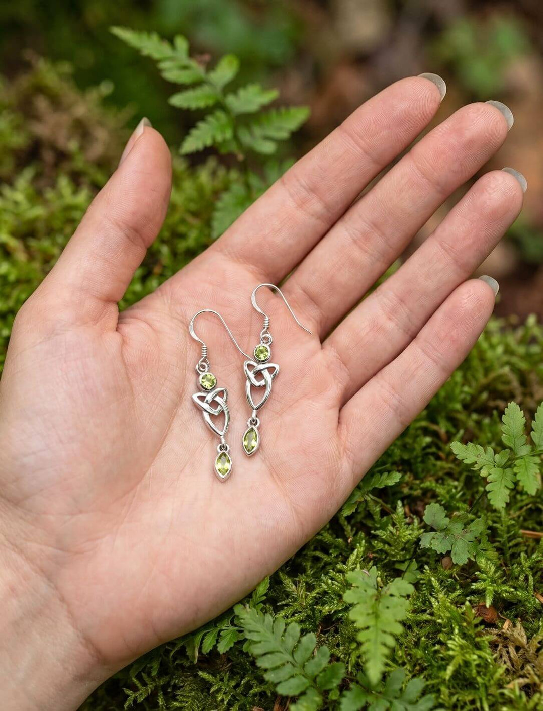 Silber Ohrhänger Triquetra mit grünem Zirkonia in der Hand über Moos