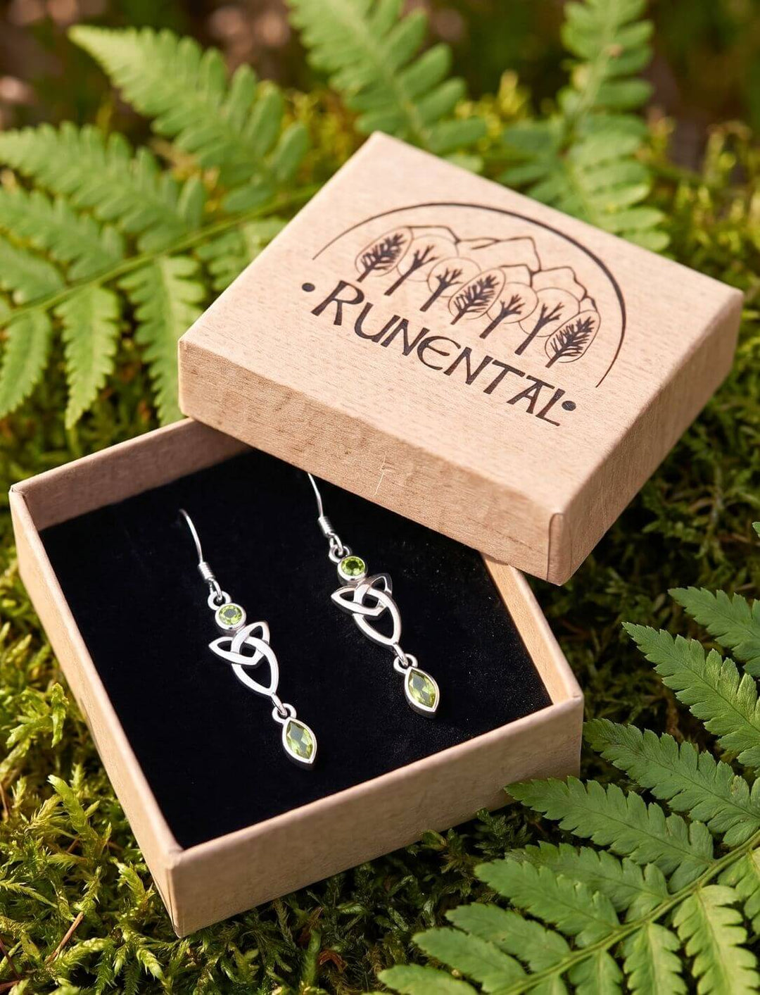 Silber Ohrhänger Triquetra mit grünem Zirkonia in geöffneter Schmuckbox auf Farn