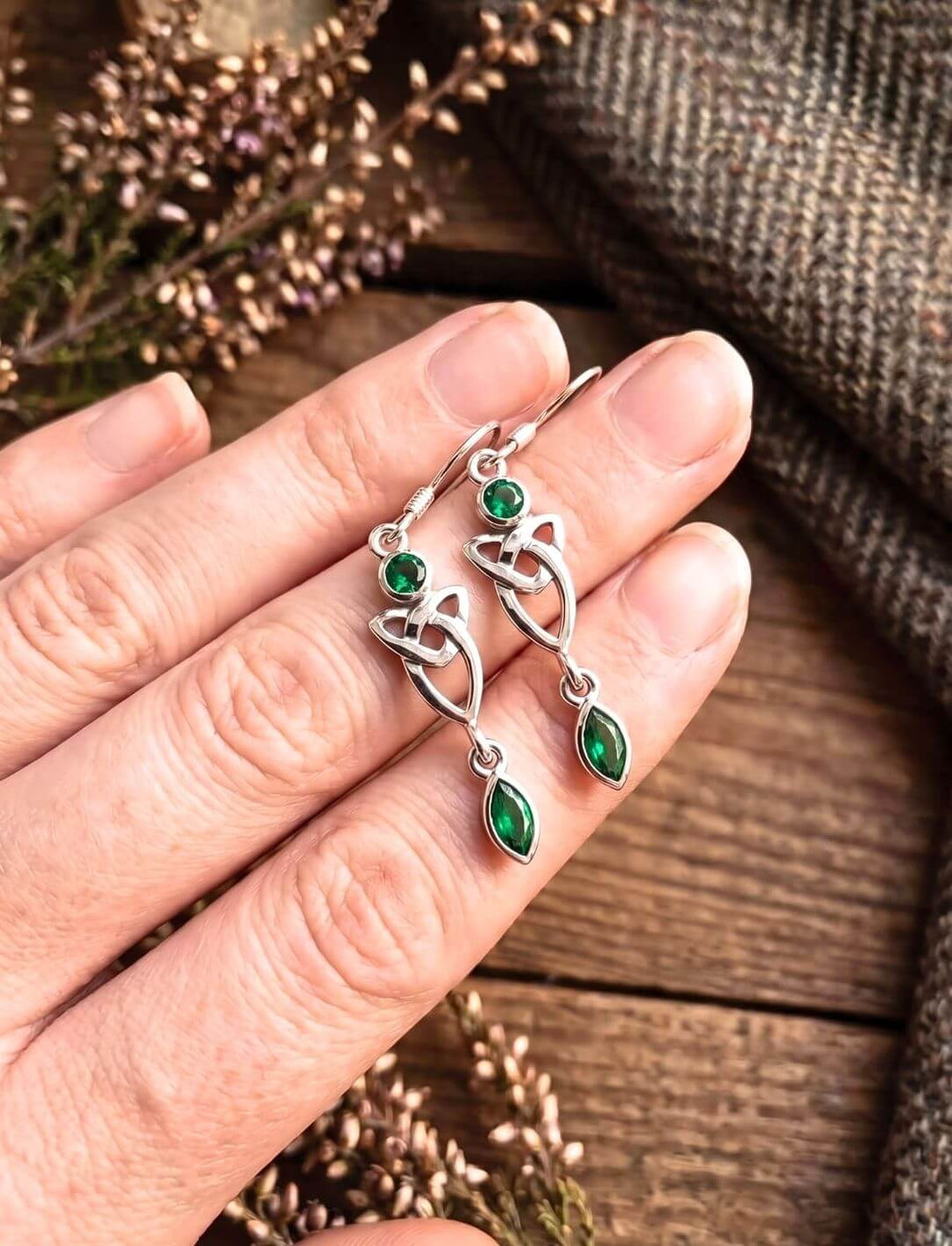 Silber Ohrhänger Triquetra mit smaragdgrünem Zirkonia in der Hand über Holz und Heidekraut