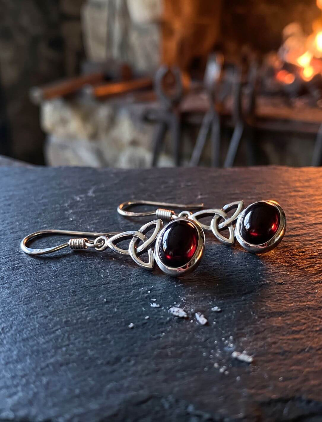 Triquetra Ohrringe aus Silber mit Granat auf einer Schieferplatte vor der Esse