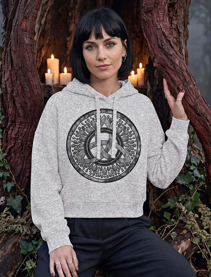 Frau im Heather Grey Triquetra Boxcut Hoodie sitzt im Kerzenschein in einem hohlen Baum