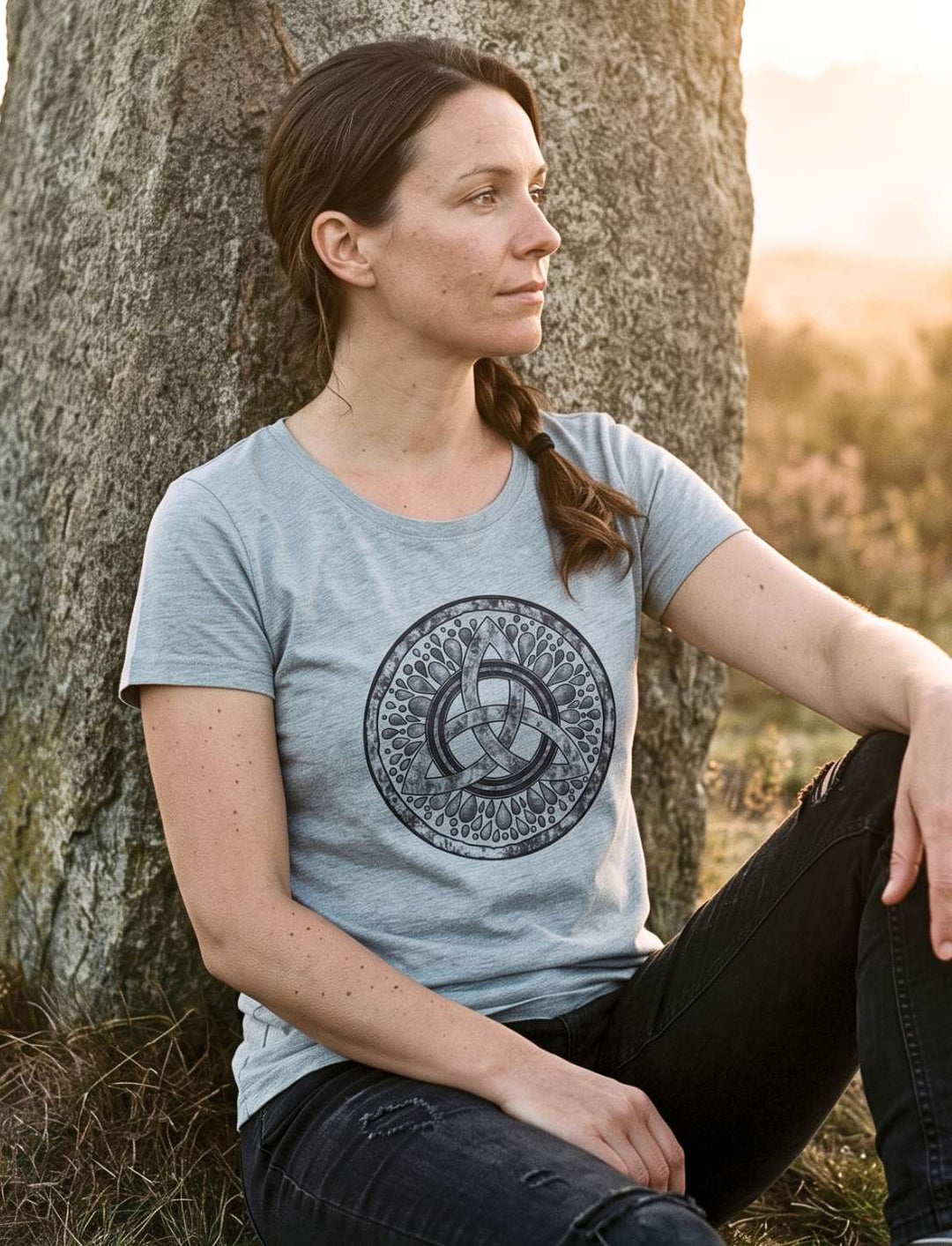 Damen T-Shirt in Heather Grey mit keltischem Motiv, Trägerin sitzt an einem Menhir bei Sonnenaufgang