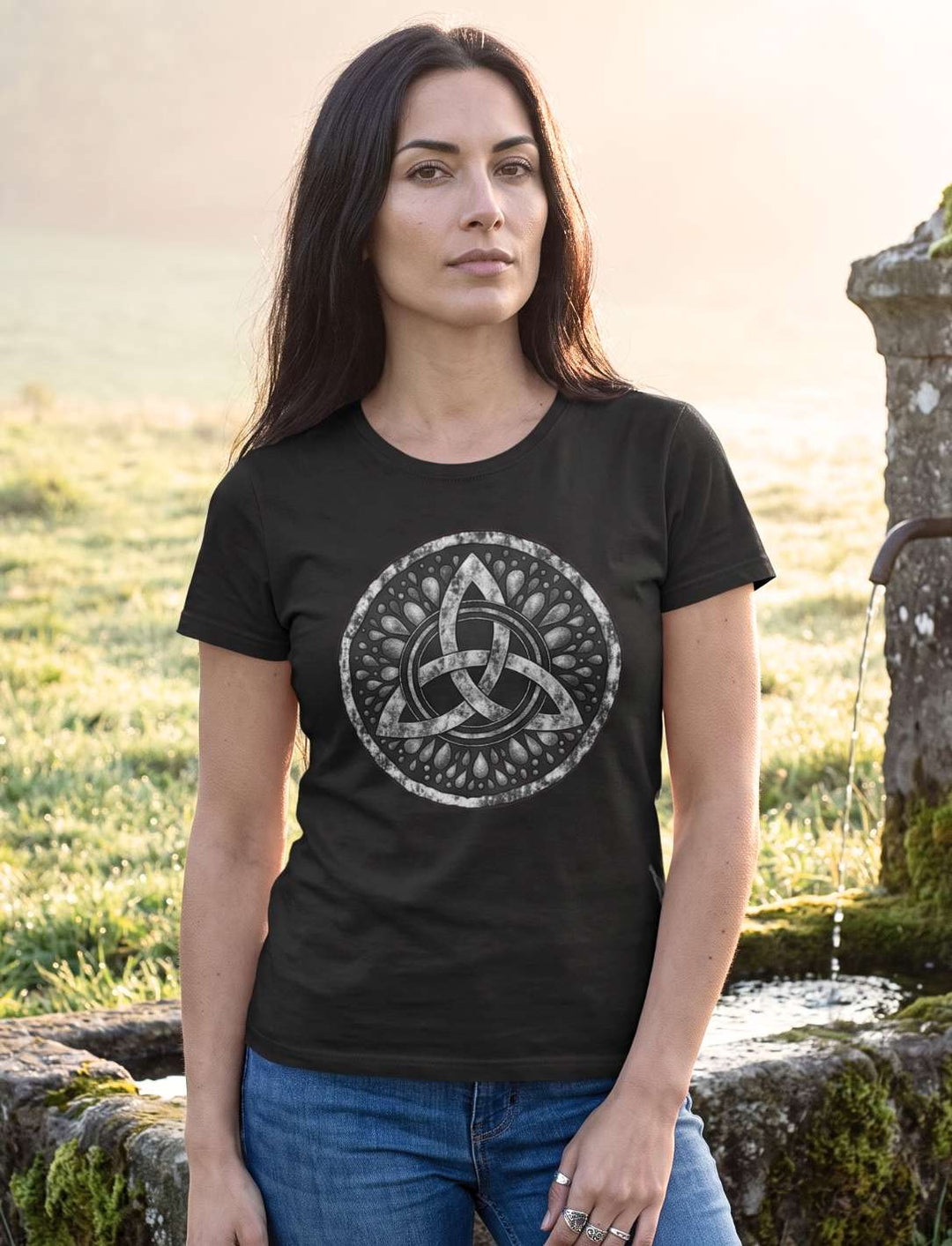Triquetra – Sichel der Seherin: Frau im schwarzen keltischen Damen Shirt an einem moosigen Quellstein im Morgennebel