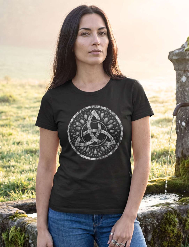 Triquetra – Sichel der Seherin: Frau im schwarzen keltischen Damen Shirt an einem moosigen Quellstein im Morgennebel