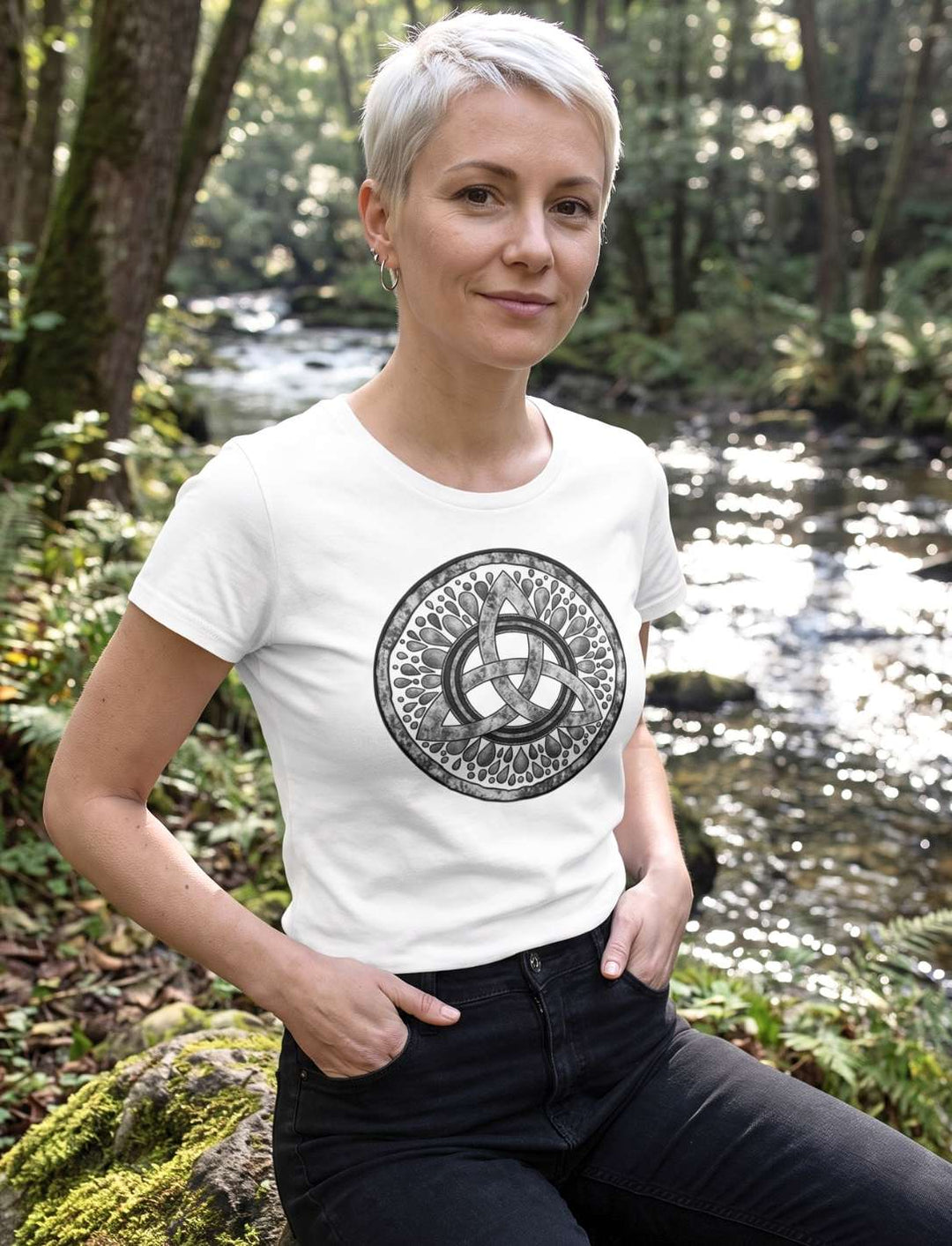Weisses Damen T-Shirt mit Triquetra-Motiv, Trägerin sitzt am Ufer eines Bachs
