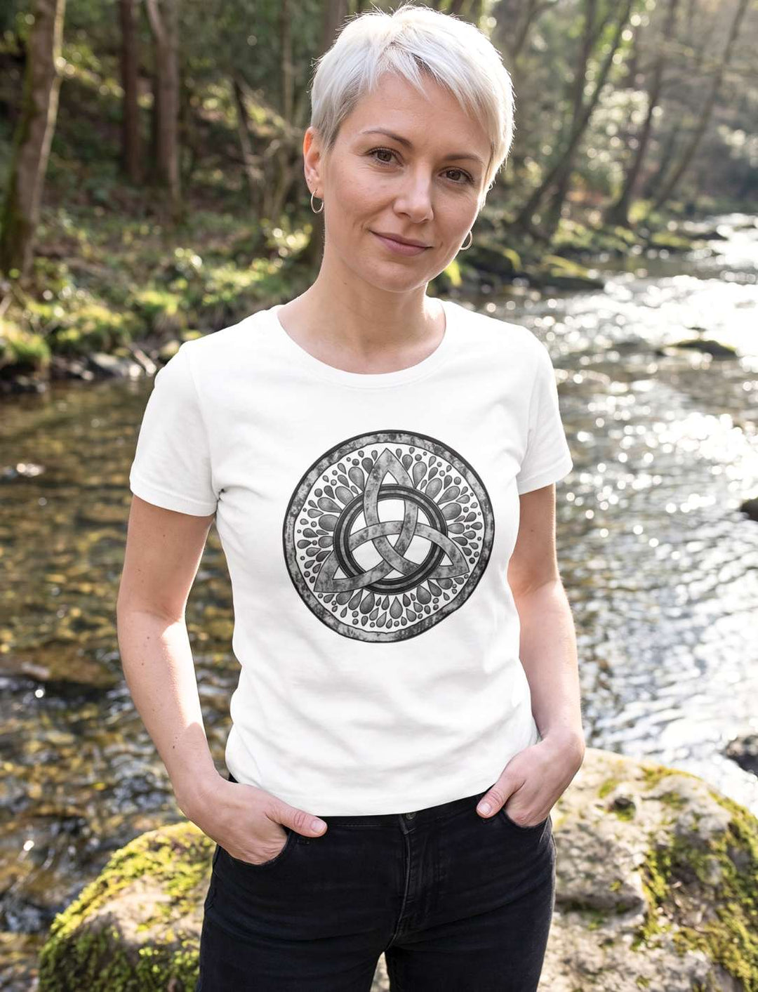 Frau mit platinblondem Kurzhaarschnitt im weissen Damen Shirt mit Triquetra am Waldbach
