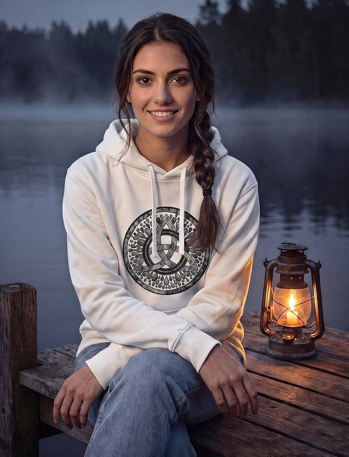 Lächelnde Frau im weißen Hoodie mit keltischem Knoten sitzt am See, neben ihr eine brennende Laterne