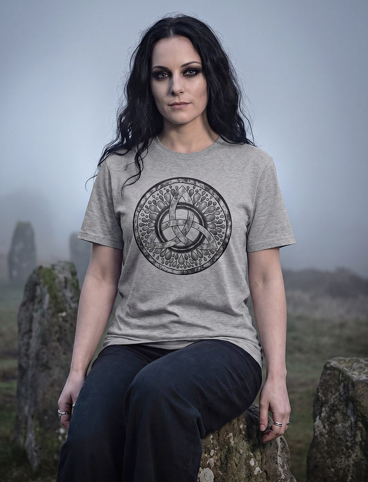 Frau im grauen Triquetra Shirt sitzt auf einem Menhir im Steinkreis, Nebel zieht hinter ihr auf