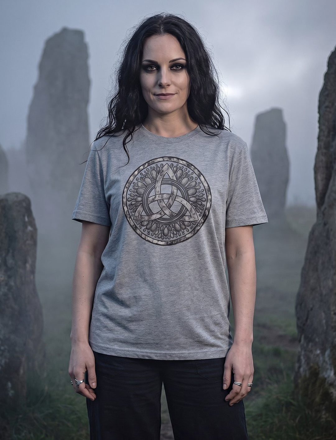 Frau im Heather Grey Damen Shirt mit Triquetra steht zwischen alten Menhiren im dichten Nebel