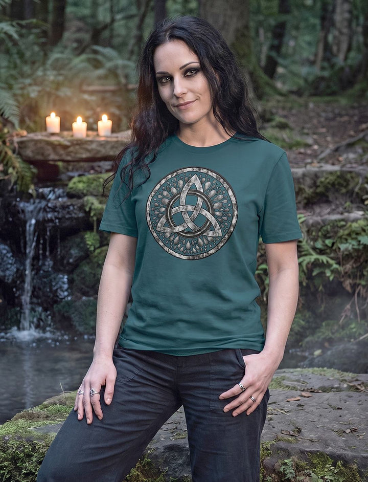 Frau im petrolblauen Stargazer Damen Shirt mit Triquetra steht vor einem kleinen Wasserfall mit Kerzen