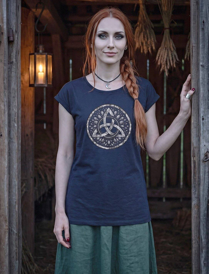 Navyblaues Damen Longshirt mit Triquetra-Motiv, Frau steht im Tor einer alten Scheune mit Kerzenlaterne