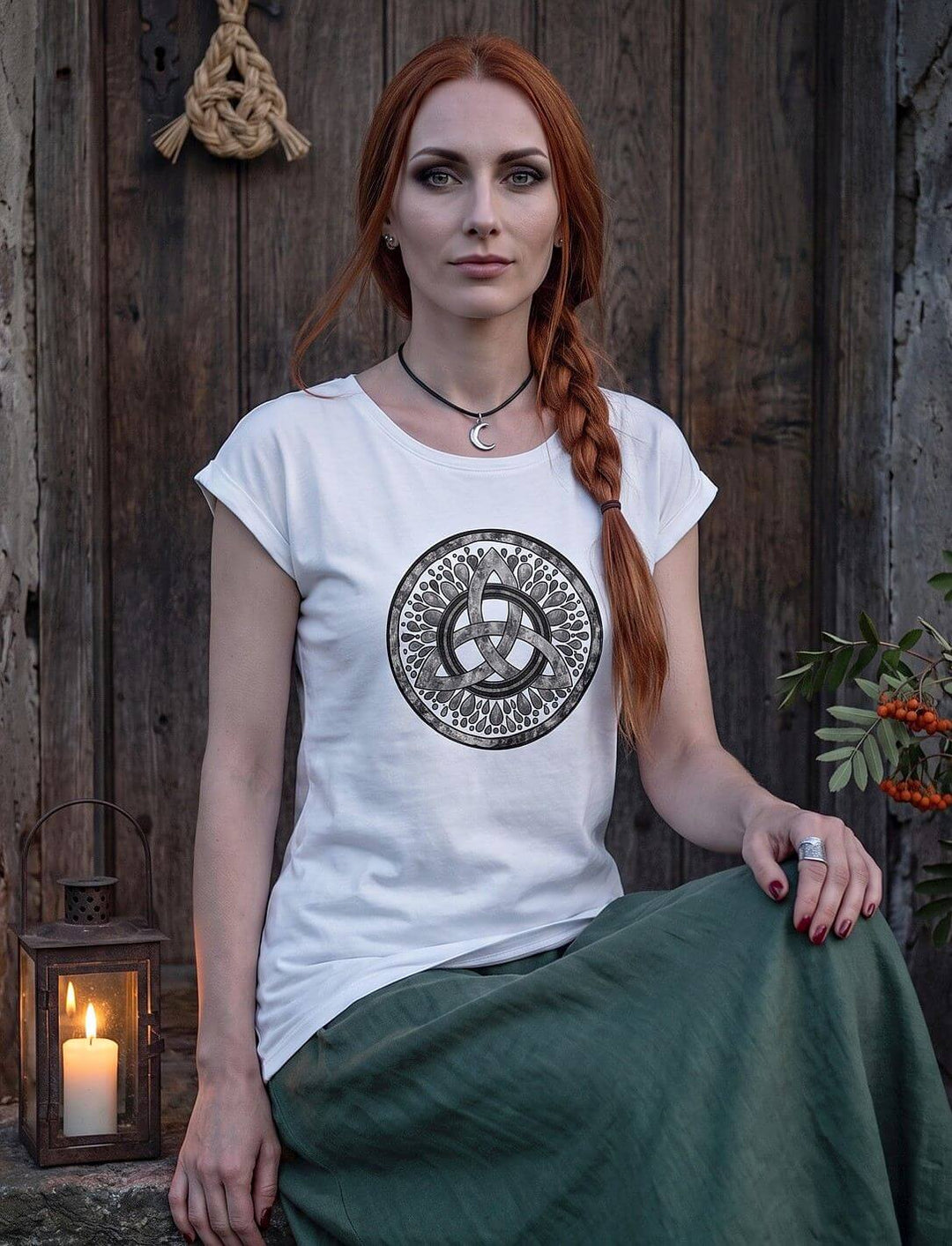 Frau im weißen Longshirt mit keltischem Knoten sitzt auf einer Steinschwelle, daneben eine Laterne mit Kerze