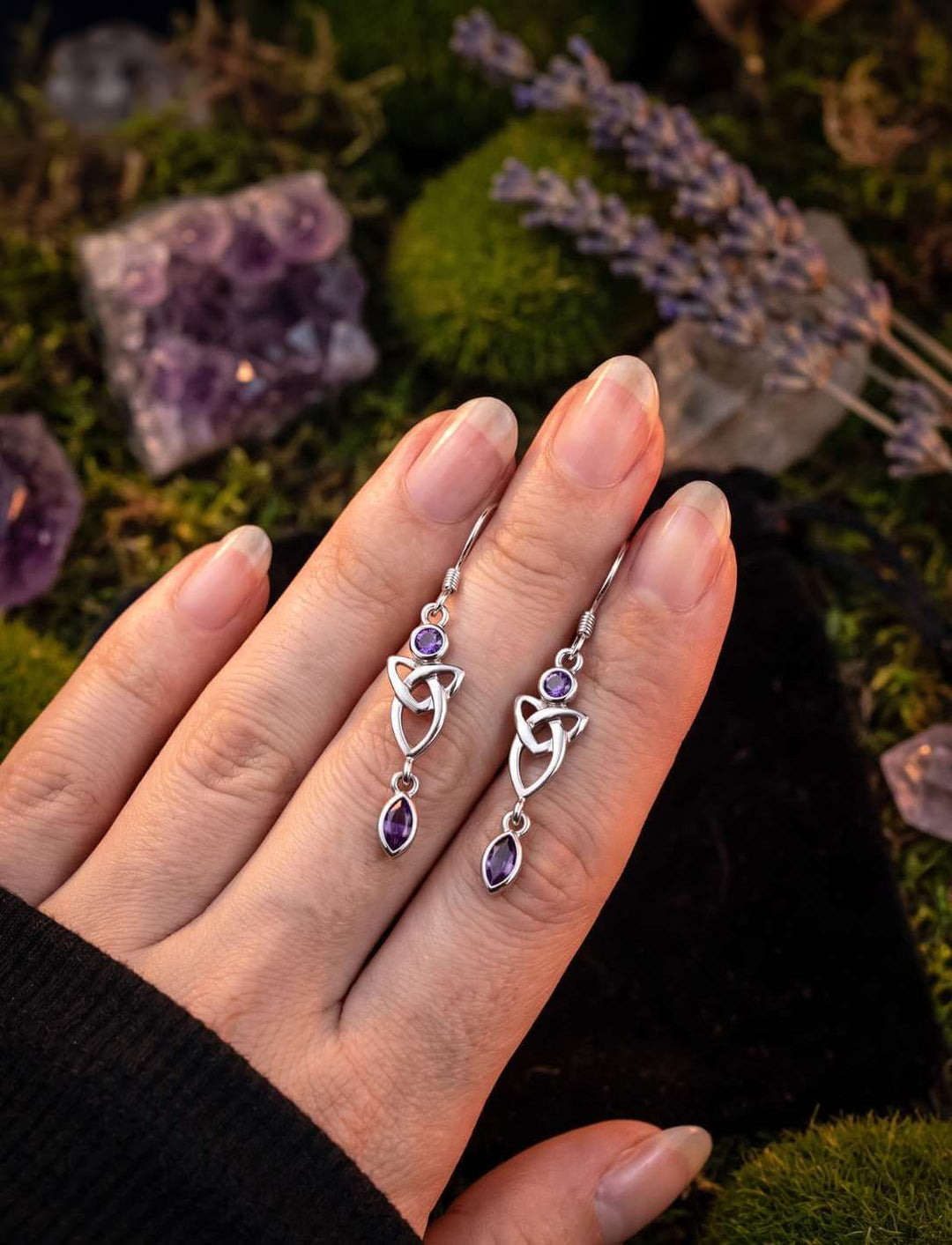 Silber Ohrhänger Triquetra mit violettem Zirkonia in der Hand auf Moos
