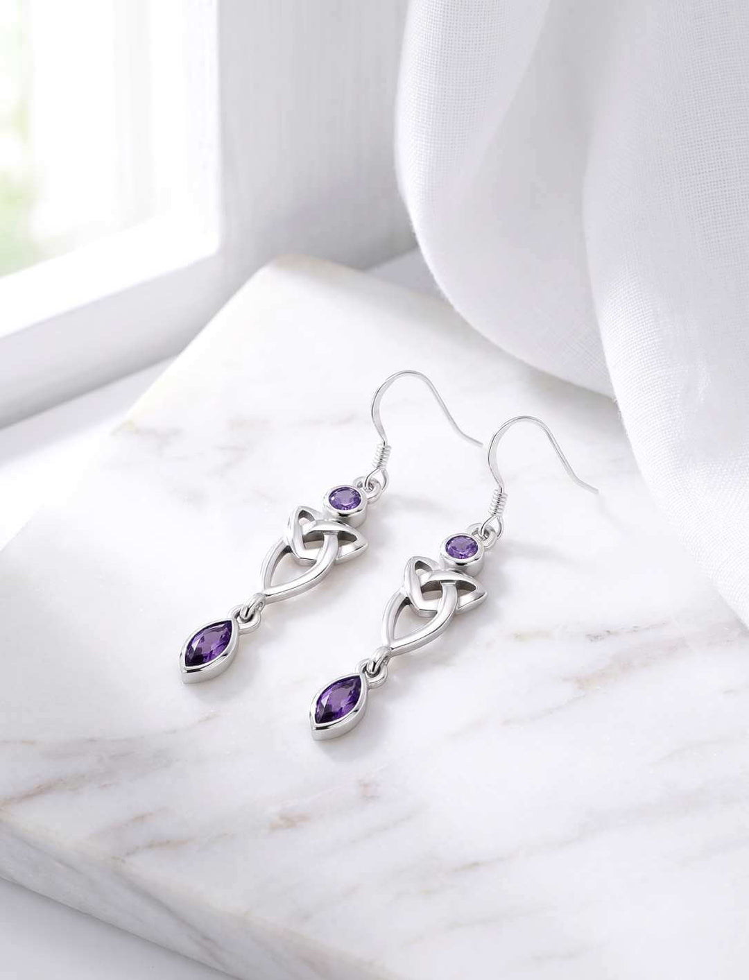 Silber Ohrhänger Triquetra mit violettem Zirkonia auf weißem Marmor Fensterbank