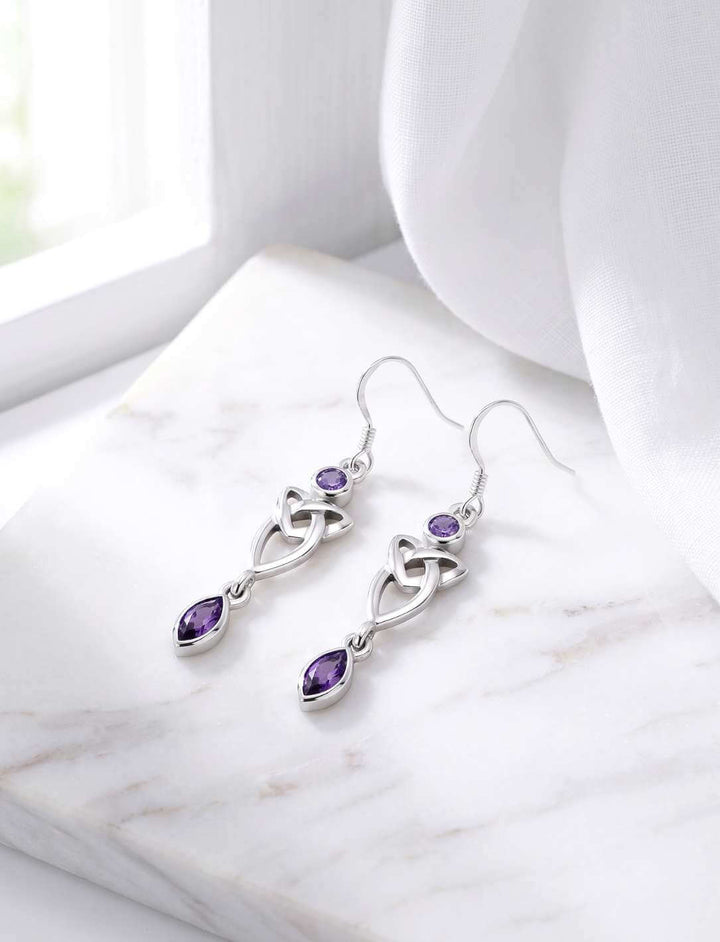 Silber Ohrhänger Triquetra mit violettem Zirkonia auf weißem Marmor Fensterbank