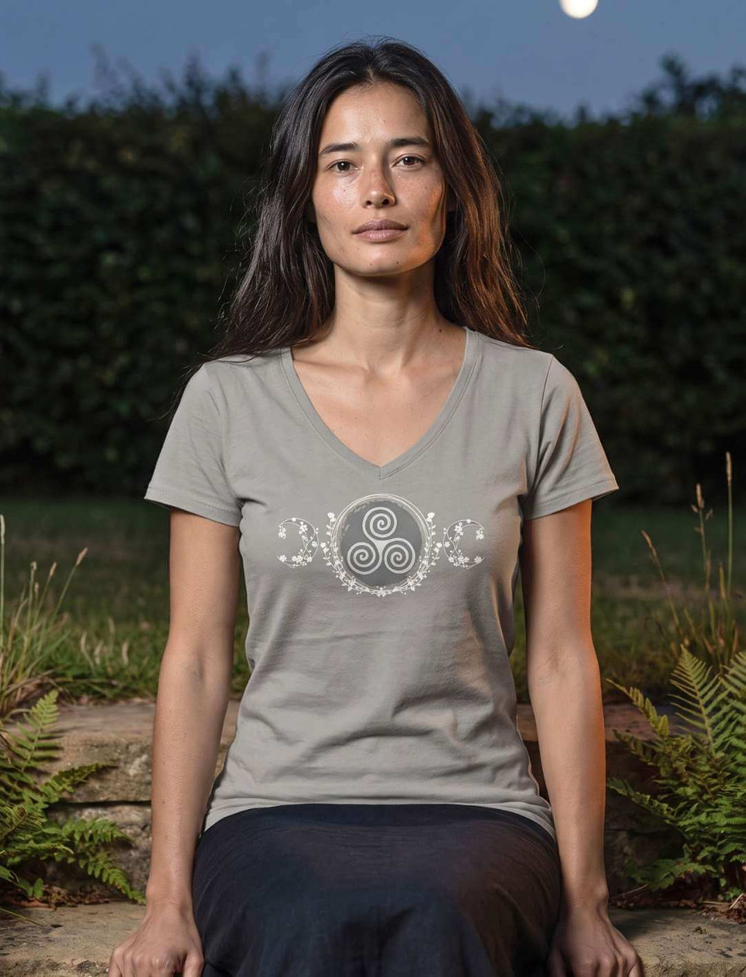 Frau sitzt in hellgrauem V-Neck Shirt auf einer Steinstufe vor dunkler Hecke