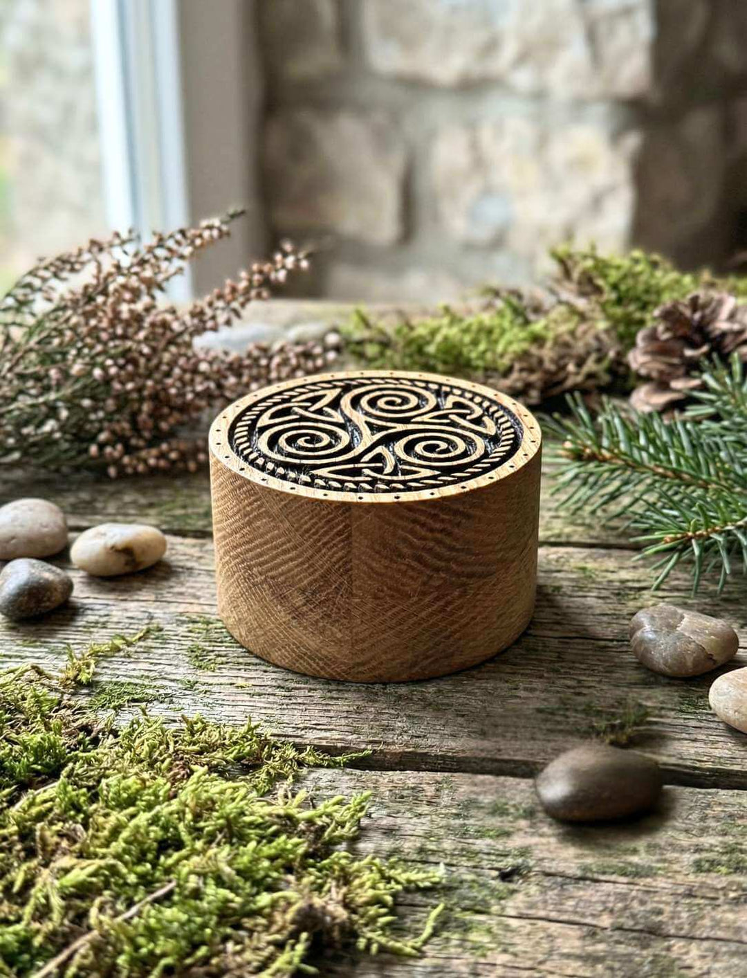 Triskele Schmuckdose aus Eichenholz geschlossen neben Tannenzweigen und Steinen
