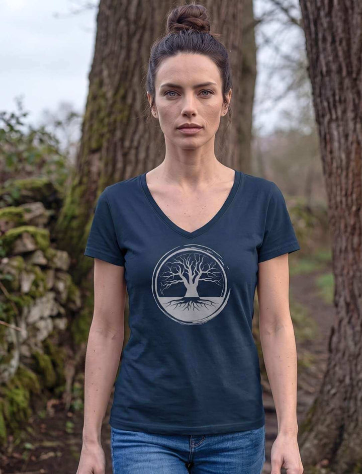 Frau in Navy V-Neck Shirt geht zwischen zwei alten Baumstaemmen hindurch