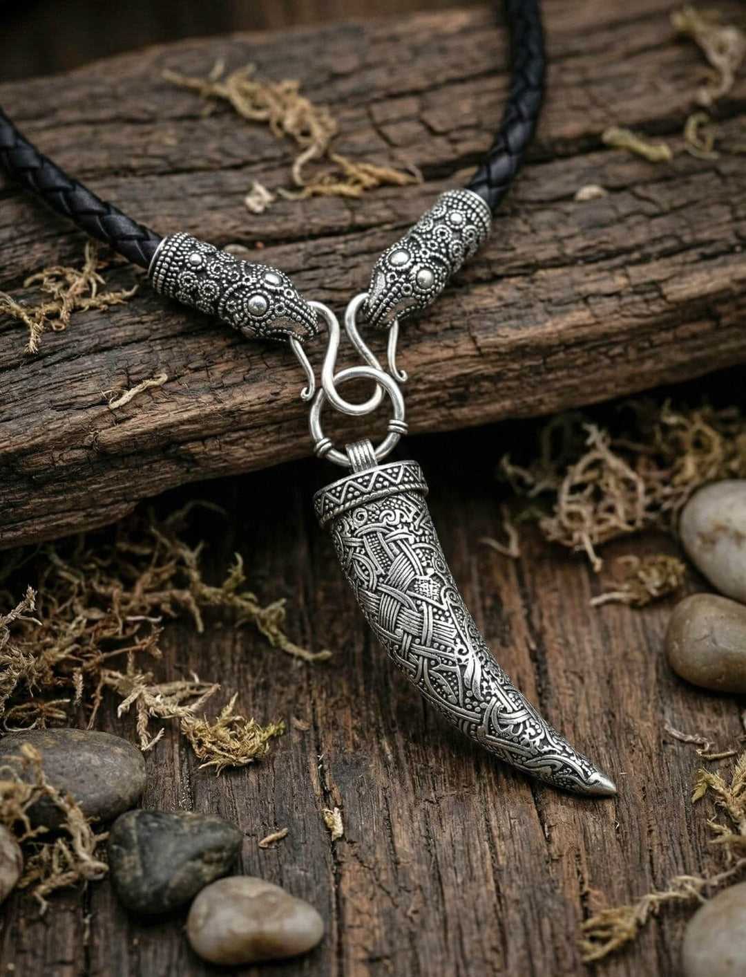 ersilberter Wolfszahn an geflochtener Lederkette mit Rabenköpfen auf altem Holz