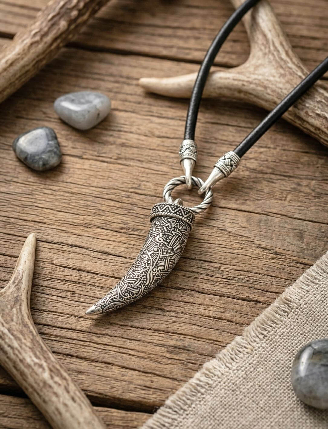 Wolfszahn-Anhänger an Lederkette mit verziertem Edelstahl-Öffnungsclip und versilberten Kettenabschlüssen auf Tierknochen.