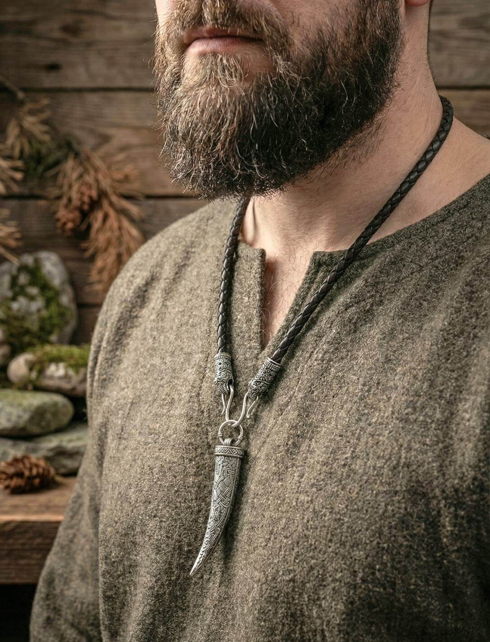 Mann in Wikinger-Tunika trägt Wolfszahn-Anhänger an geflochtener Lederkette mit Rabenkoepfen